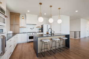Kitchen featuring dark countertops, a kitchen island with sink, a kitchen breakfast bar, backsplash, and open shelves