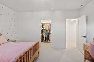 Bedroom with light colored carpet and a walk in closet