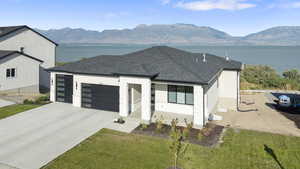 View of front of home with roof with shingles, a garage, concrete driveway, a water and mountain view, and a front lawn