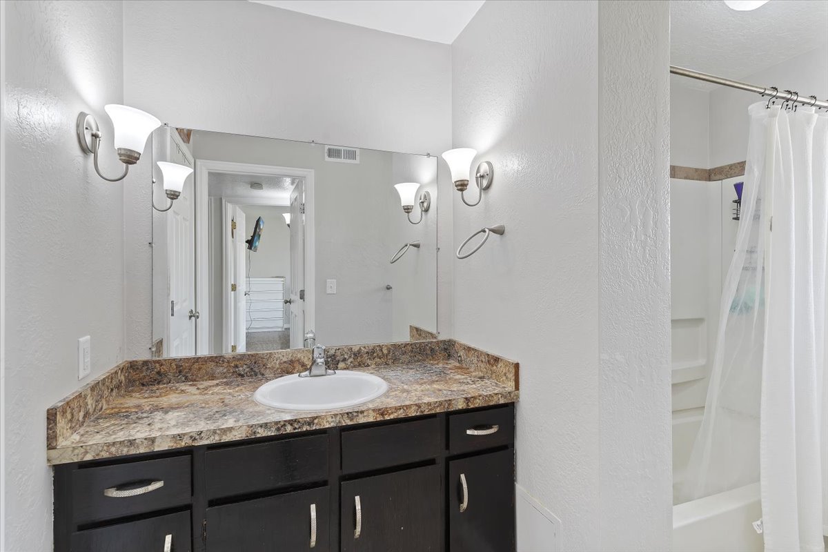Full bathroom featuring vanity, a textured wall, and shower / tub combo