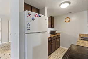 Kitchen featuring dark wood finish cabinets, black appliances, a textured ceiling, and light tile patterned floors