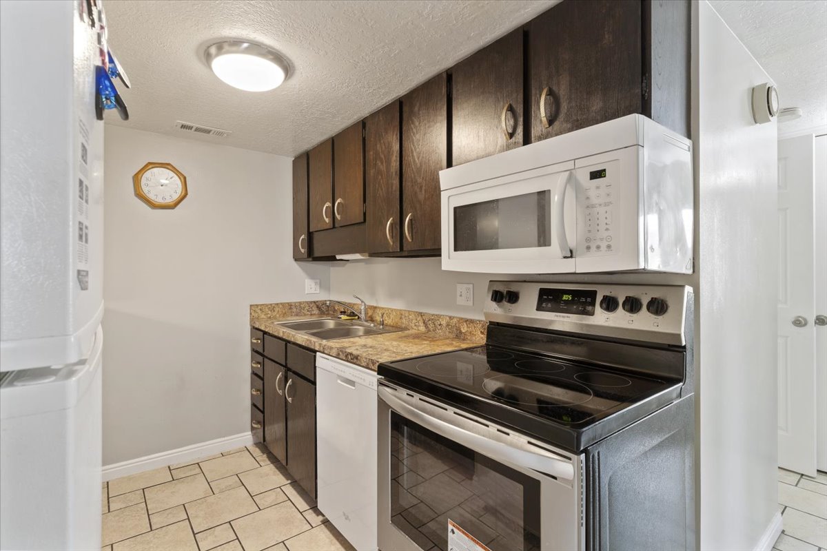 Kitchen with white appliances, dark wood finish cabinetry, a textured ceiling, light countertops, and light tile patterned floors
