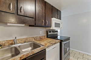 Kitchen featuring dark wood finish cabinetry, white appliances, a textured ceiling, and light tile patterned flooring