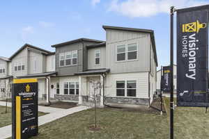 View of front of house featuring board and batten siding, stone siding, and a front lawn