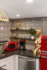 Kitchen with white cabinetry, stainless steel dishwasher, tasteful backsplash, and dark stone countertops