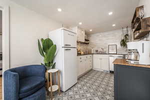 Kitchen with wood counters, freestanding refrigerator, open shelves, stainless steel dishwasher, and backsplash