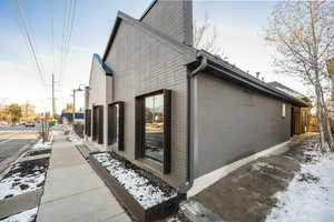 View of snow covered exterior with a chimney and brick siding