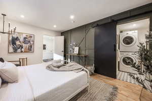Bedroom featuring a barn door, ensuite bath, wood finished floors, stacked washer / drying machine, and a chandelier