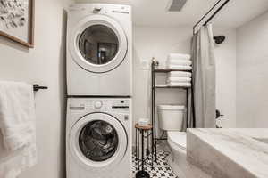 Full bath with stacked washing machine and dryer, shower / bathtub combination with curtain, and tile patterned flooring