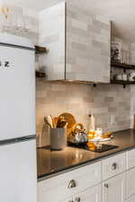 Kitchen featuring open shelves, freestanding refrigerator, white cabinets, dark stone counters, and backsplash