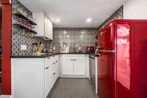 Kitchen featuring open shelves, freestanding refrigerator, white cabinets, dark tile patterned floors, and dark stone counters