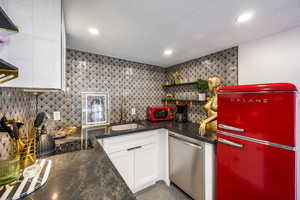 Kitchen with freestanding refrigerator, open shelves, dark stone countertops, white cabinetry, and dishwasher