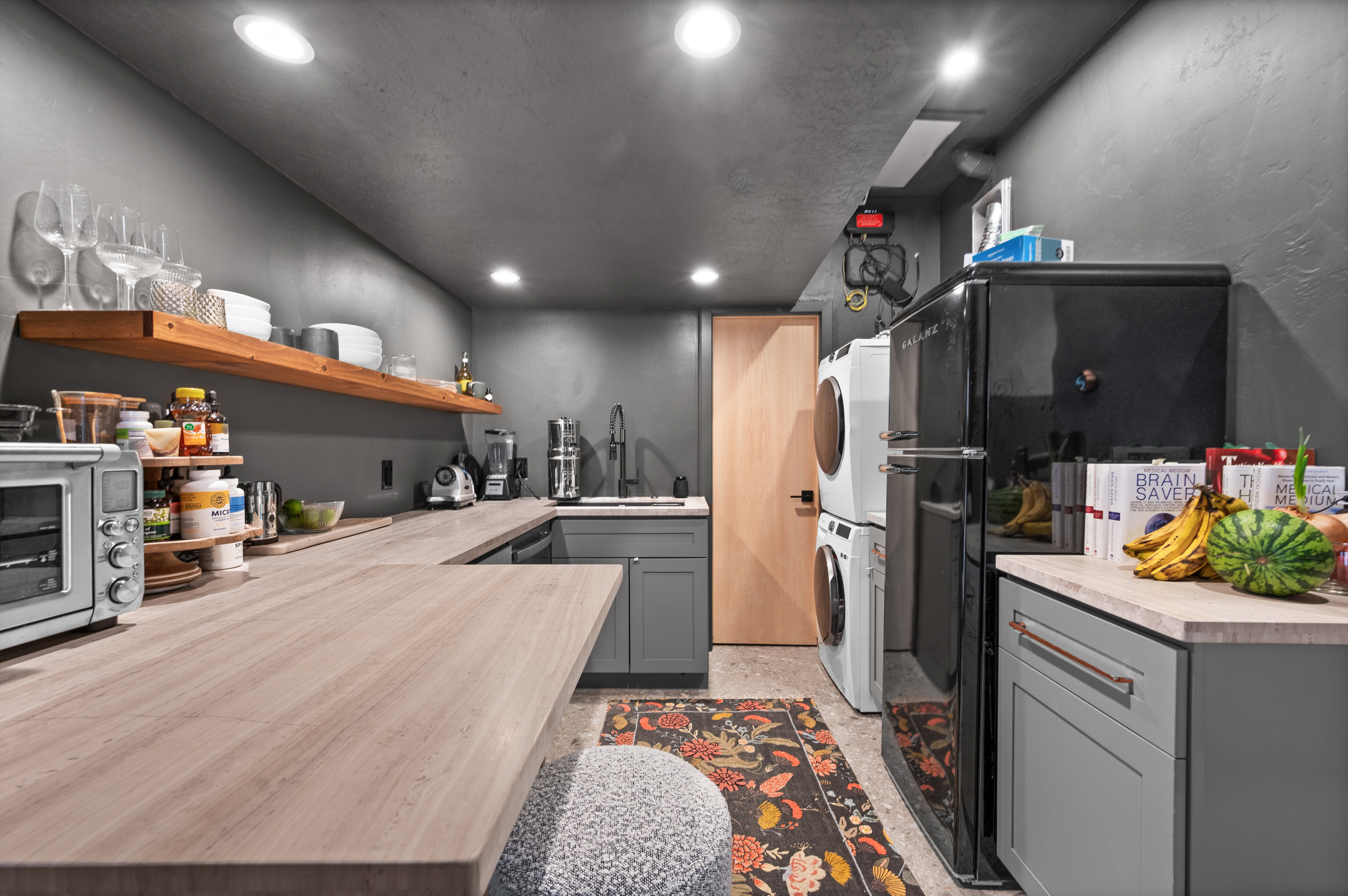 Kitchen featuring gray cabinets, freestanding refrigerator, recessed lighting, open shelves, and stacked washer / dryer