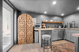 Bar area with gray cabinets, stainless steel dishwasher, open shelves, and recessed lighting