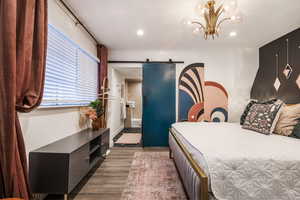 Bedroom featuring a barn door, ensuite bath, light wood-style flooring, and suspended lighting