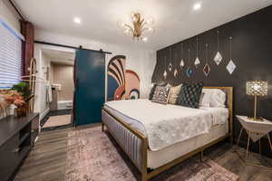 Bedroom featuring a barn door, dark wood-style flooring, a chandelier, and connected bathroom