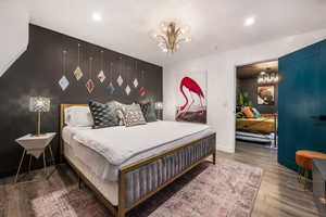Bedroom featuring an accent wall, suspended lighting, and wood finished floors