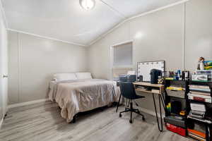 Bedroom featuring an office area, light wood-type flooring, lofted ceiling, and ornamental molding