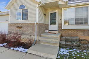 Snow covered property entrance with brick siding and an attached garage