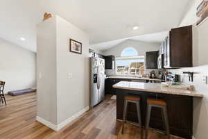 Kitchen with a breakfast bar, stainless steel appliances, lofted ceiling, light stone counters, and a peninsula