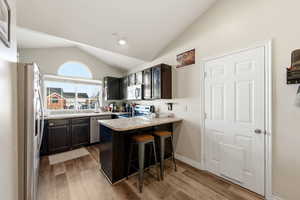 Kitchen featuring a breakfast bar area, stainless steel appliances, a peninsula, lofted ceiling, and light wood-style flooring