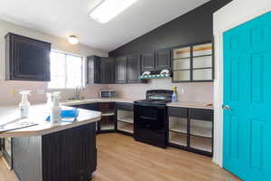 Kitchen with electric range, a peninsula, light countertops, lofted ceiling, and light wood-type flooring