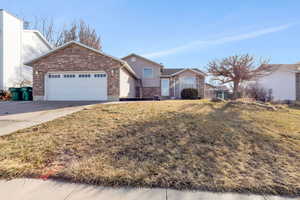 Ranch-style home featuring a front lawn, concrete driveway, a garage, and brick siding