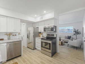 Kitchen with stainless steel appliances, wood tiled floors, white cabinetry, light stone counters, and recessed lighting