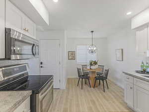 Kitchen with stainless steel appliances, white cabinets, wood tiled floors, light stone counters, and a chandelier