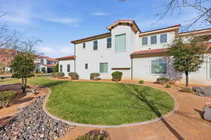 Rear view of property featuring a yard, stucco siding, and a tiled roof