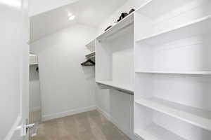 Walk in closet with light colored carpet and lofted ceiling