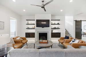 Living area with a barn door, light tile patterned floors, ceiling fan, recessed lighting, and a fireplace