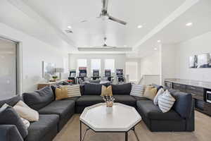 Living area with a tray ceiling, ceiling fan, light colored carpet, and recessed lighting