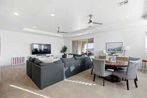 Living room featuring light colored carpet, ceiling fan, recessed lighting, and a tray ceiling