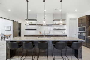 Kitchen featuring open shelves, light tile patterned floors, dark wood finish cabinets, and a kitchen breakfast bar