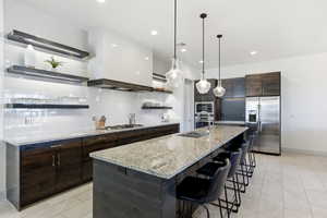 Kitchen featuring open shelves, dark wood finish cabinetry, decorative backsplash, stainless steel appliances, and light stone countertops