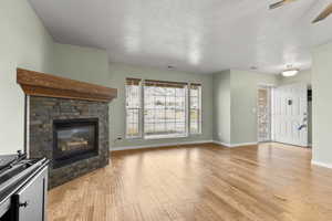 Unfurnished living room with a glass covered fireplace, light wood-style floors, a textured ceiling, and ceiling fan