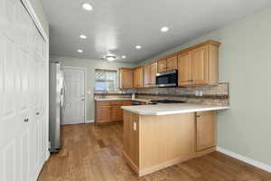 Kitchen with a peninsula, light countertops, stainless steel appliances, light wood-type flooring, and a textured ceiling