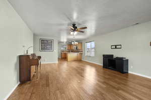 Living room featuring light wood finished floors, ceiling fan, hanging lights, and a textured ceiling