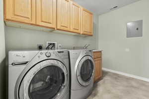 Laundry room with finished concrete flooring, electric panel, cabinet space, and washing machine and clothes dryer