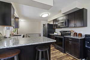 Kitchen featuring a kitchen breakfast bar, black appliances, light stone counters, and dark wood finish cabinetry