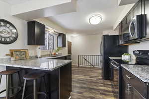 Kitchen with stainless steel appliances, light stone counters, a peninsula, a breakfast bar, and dark wood-style flooring