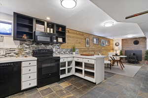 Kitchen featuring black appliances, a peninsula, light countertops, a wood stove, and dark stone finish flooring