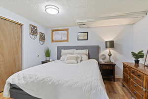 Bedroom with a textured ceiling, wood finished floors, and a closet