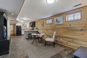 Dining area with wood walls, dark stone finish floors, and a textured ceiling