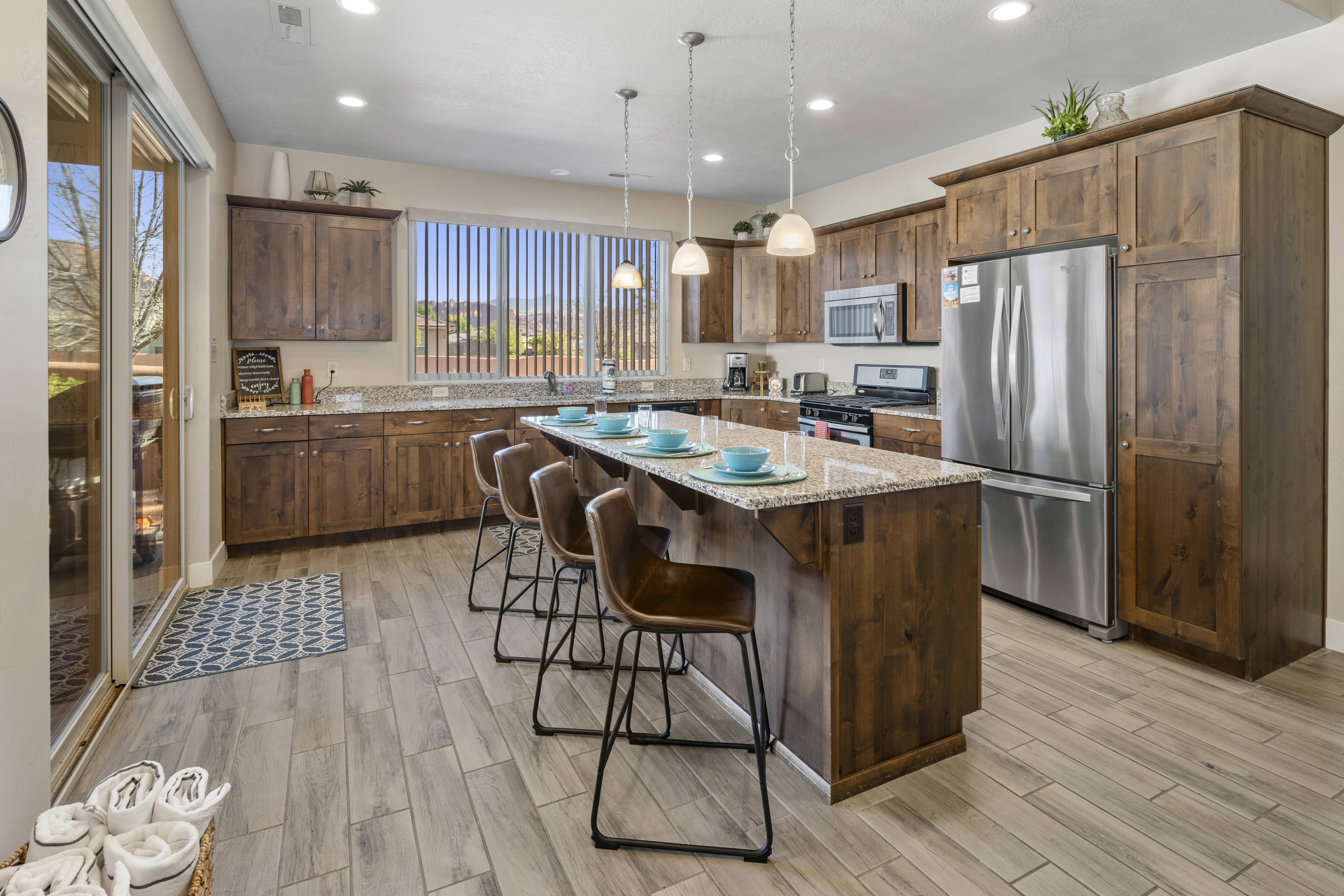 Kitchen featuring stainless steel appliances, light stone counters, hanging light fixtures, a kitchen island, and wood tiled floors