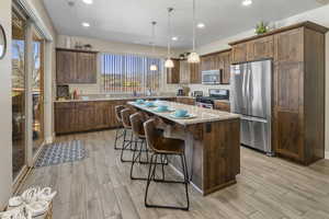 Kitchen featuring stainless steel appliances, light stone counters, hanging light fixtures, a kitchen island, and wood tiled floors