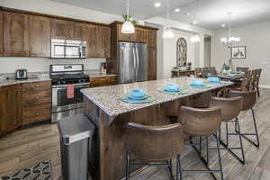 Kitchen featuring stainless steel appliances, a center island, light stone counters, and wood tiled floors