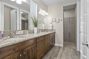 Primary Bathroom with double vanity, a tile shower, and wood finish floors