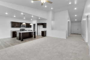 Kitchen with a ceiling fan, dark wood finish cabinetry, open floor plan, a kitchen breakfast bar, and light carpet